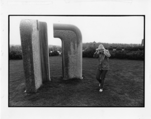A student poses next to the "Portal" sculpture in the middle of a rainstorm. This picture helps to demonstrate the scale of the sculpture.